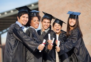 Portrait of happy students in graduation gowns showing diplomas